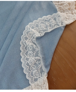 Macro shot of light blue tablecloth featuring delicate white lace edge on wooden table
