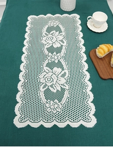 Detail of white lace table runner with hollowed rose floral patterns on green fabric