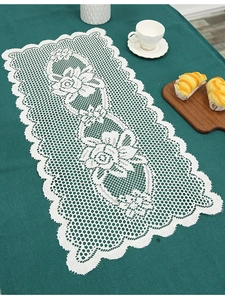 Detail of white rectangle lace table runner with floral embroidery on a dark green table