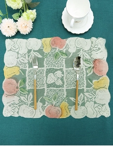 Lace placemat detail with colorful fruit prints and scalloped edges on dark table