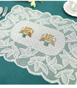 Detailed view of rectangular white lace placemat with yellow flower embroidery on green cloth