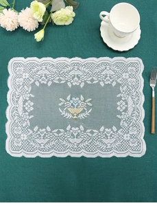 Close-up of a white round lace placemat with blue and yellow floral embroidery on table