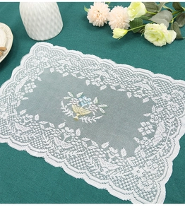 Detailed embroidery of a floral basket on a white lace rectangle table mat with scalloped edges