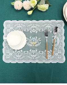 Close-up of white lace placemat with colorful floral basket embroidery on green table