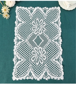 Detailed view of white rectangular lace placemat with floral embroidery on blue background