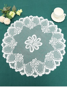 Close-up of circular white lace placemat with floral embroidery on deep green velvet fabric