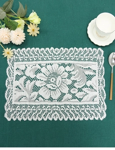 Macro detail of white lace placemat with floral embroidery on a dark green background
