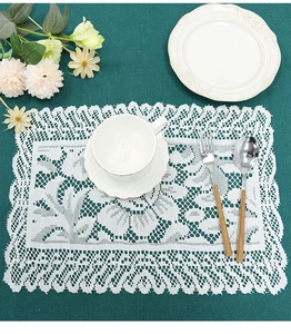 Close-up of white lace placemat with floral hollow patterns on green tablecloth