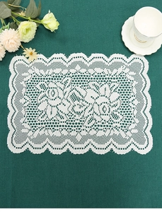 Detail of white vintage lace placemat with floral embroidery on dark green fabric