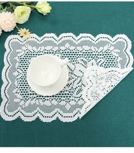 Detail of white lace round placemat with intricate floral crochet patterns on green cloth