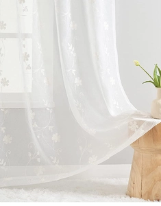 Close-up of white sheer curtain featuring delicate vine and floral embroidery detail