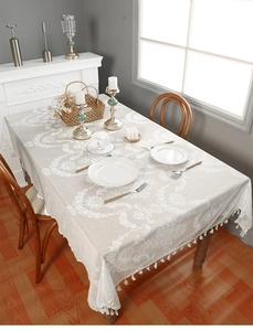 Detailed view of white floral lace tablecloth with elegant ball fringe on wooden dining table