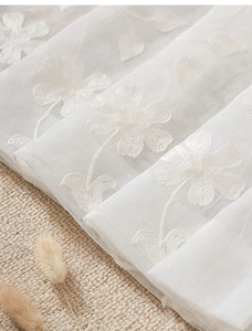 Detail of white semi-transparent floral embroidery on lightweight rustic window curtain