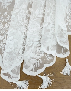 Detail of white French lace curtain with elegant floral embroidery and tassel fringe