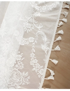 Close-up of white lace tablecloth featuring delicate floral embroidery and fringed edges