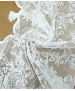 Detail of white rose lace curtain featuring delicate floral embroidery and fringed tassels