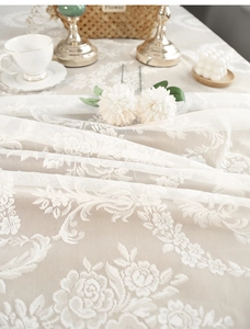 Detail of white French lace tablecloth featuring delicate rose embroidery and soft fringe