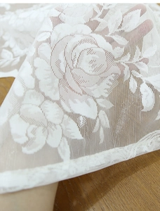 Close-up of white rose lace fabric with delicate floral mesh patterns and wavy edges