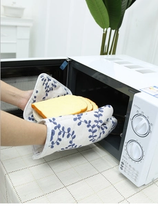 Close-up of thick oven mitts with blue leaf patterns taking toast from a microwave