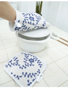 Close-up of a floral oven mitt lifting a ceramic pot lid on a checkered tablecloth