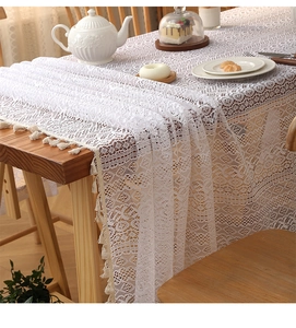 Close-up of white lace tablecloth with geometric patterns and fringe on a wooden table