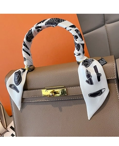 Detail of printed silk scarf wrapped on brown leather handbag handle with gold lock