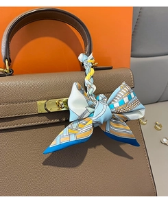 Detail of silk twilly scarf with chain print wrapped as a bow on brown leather bag handle