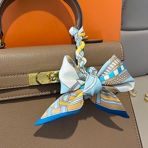 Elegant silk twill narrow scarf with geometric print tied as a bow on a leather bag handle