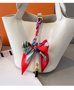 Detail eines Seidenschals, der als Schleife am Griff einer weißen Ledertasche gebunden ist