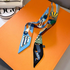 Detail eines Seidenschals mit geometrischem Muster und Paris-Logo in einer orangefarbenen Box