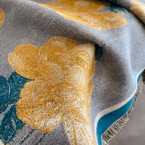 Detail of woven floral scarf with retro grey-blue and yellow patterns and fringed edges