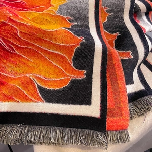Detail view of woven autumn maple leaf pattern on thick scarf with orange fringe trim