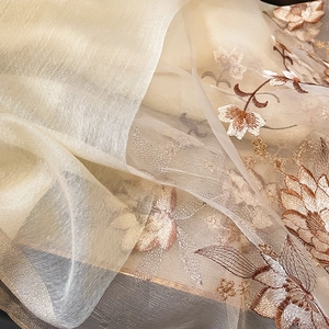 Détail macro d'une broderie florale délicate sur une écharpe en soie et laine champagne