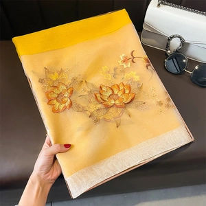 Détail d'une écharpe en soie et laine jaune avec broderie florale dorée et bord contrasté
