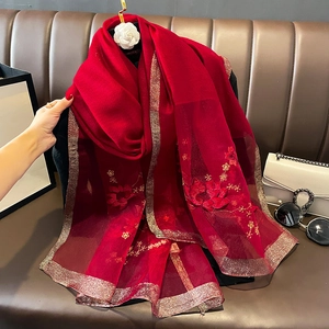 Détail d'une écharpe en soie et laine rouge avec bord doré brillant et broderie