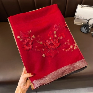 Détail d'une écharpe en soie et laine rouge avec broderies florales et bords scintillants