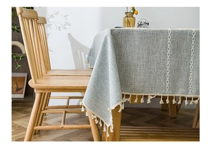 Detail of grey-green linen tablecloth featuring white cross embroidery and short tassels
