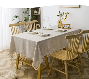 Detail of beige linen tablecloth featuring white geometric embroidery and tassel trim