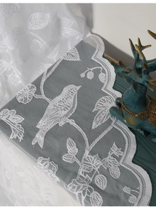 Detail of white lace curtain with delicate bird and leaf embroidery and scalloped edges