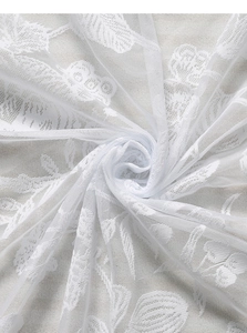 Close-up of white lace curtain fabric with delicate floral embroidery and mesh texture