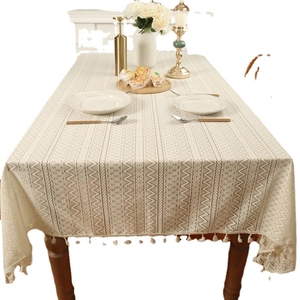 Bohemian cream lace tablecloth with geometric cutouts and tassels on wooden table