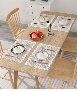 Set of four white lace placemats with hollow-out floral pattern on a wooden table