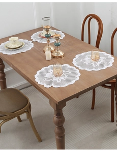 Set of four round white lace placemats with floral embroidery on a wooden table