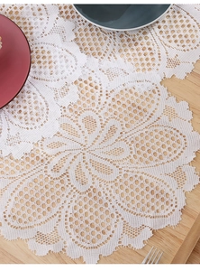 Detail of white floral lace placemat featuring intricate hollow knitting on wooden table