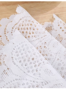 Detail of white hollow lace placemat with floral mesh patterns on a wooden surface