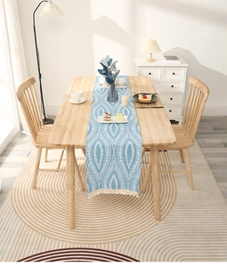 Close-up of light blue chenille table runner with white geometric leaf patterns and tassels