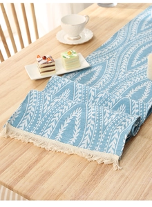 Close-up of light blue table runner with woven leaf patterns and cream tassels