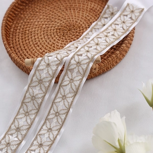 Cinta de encaje blanco con bordado floral dorado sobre una bandeja con textura