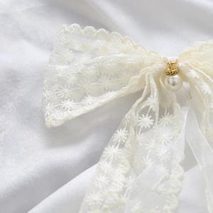 Primer plano de lazo de encaje beige con bordado de margaritas, perlas y diamantes