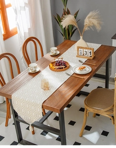 Detail of beige table runner with taupe geometric patterns and cream tassels on wood